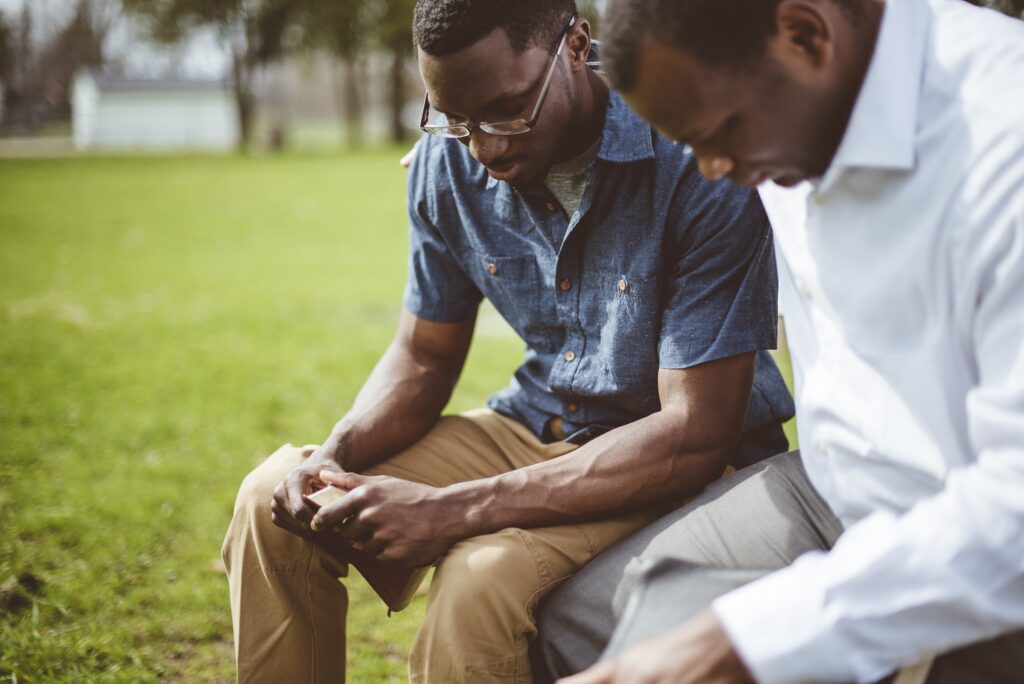 African-American male friends sitting and praying with closed eyes and the Bible in their hands